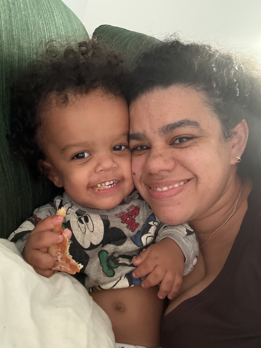 Isaiah, a smiling little boy with curly hair, cuddled up with his mum